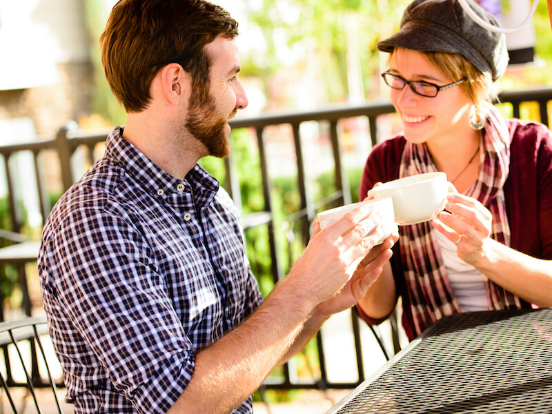 A happy male, wearing hearing aids, sitting with a female for coffee. Focus is on the hearing aid.