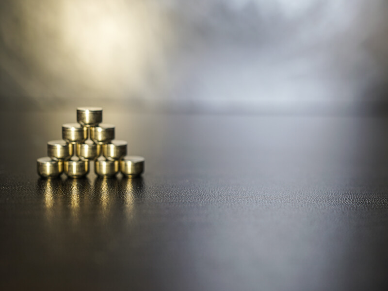 Button battery for hearing aids on the brown wooden table. The object is on the left. The batteries are stacked in a triangle.
