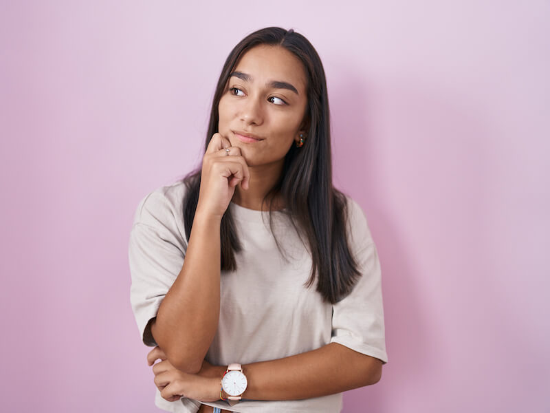Woman standing in front of a pink backdrop wondering is seeing a hearing specialist is her best option for hearing aids.