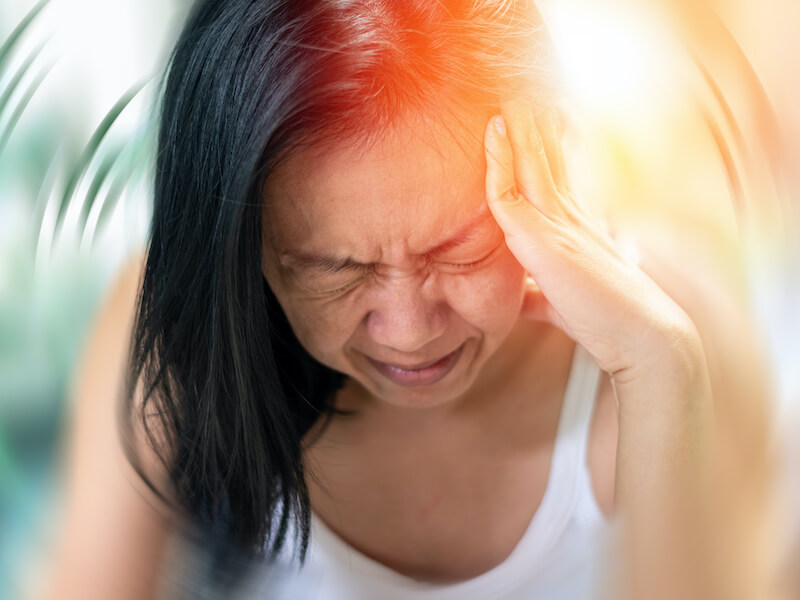 Woman grimacing with hand on the left side of her head suffering from tinnitus