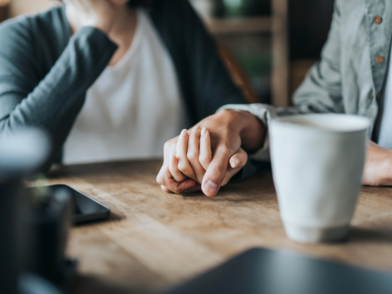 Couple on a date in cafe, holding hands on coffee table having a discussion about hearing loss and how its effecting their relationship. Two cups of coffee and smartphone on wooden table. Love and care concept.