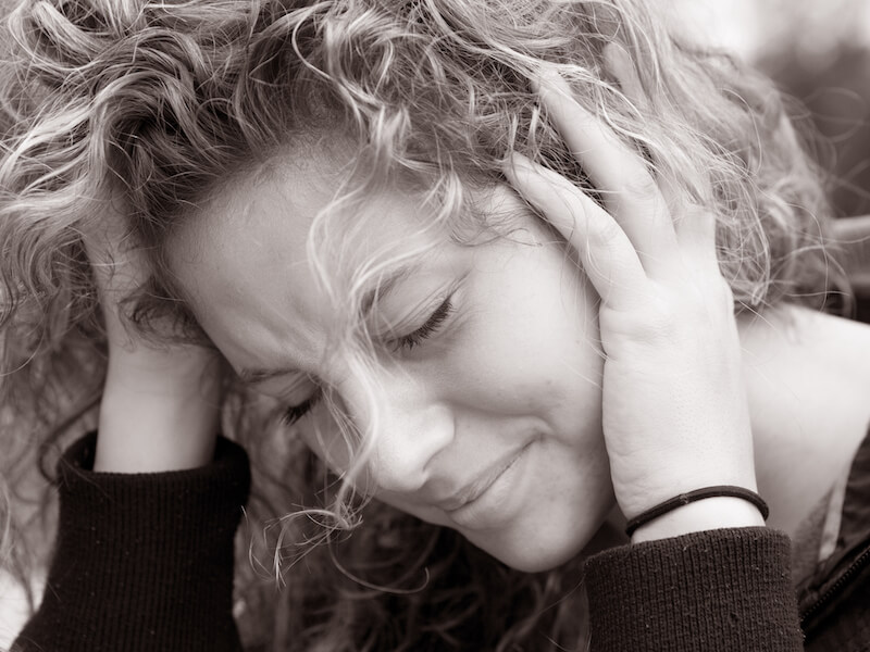 Woman holding her head from ringing in the ears and looking depressed.