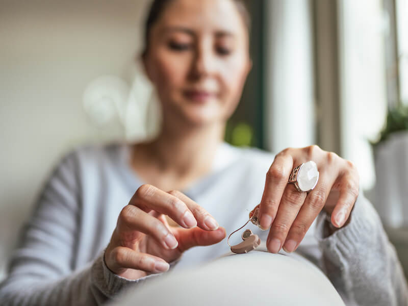 Woman putting on her hearing aid over the couch in case she drops it.