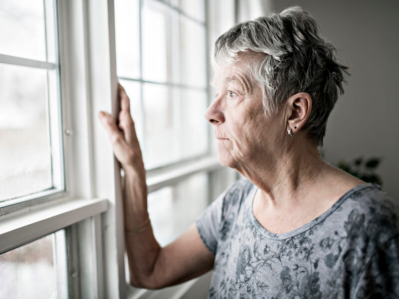 Woman at the window looking out and feeling isolated from untreated hearing loss.