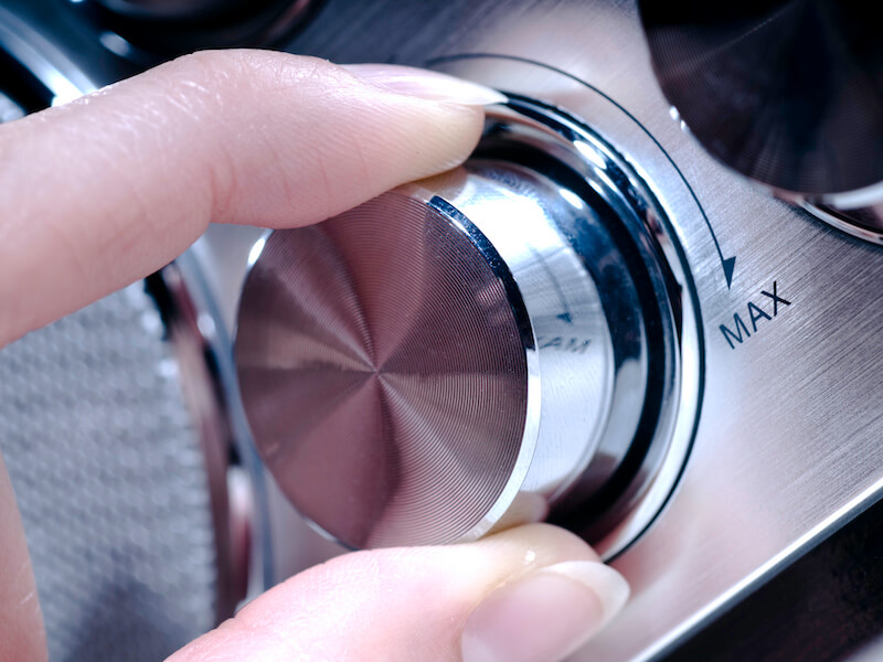 Female hand adjusting the radio volume dial to max on a silver radio because she can't hear it.