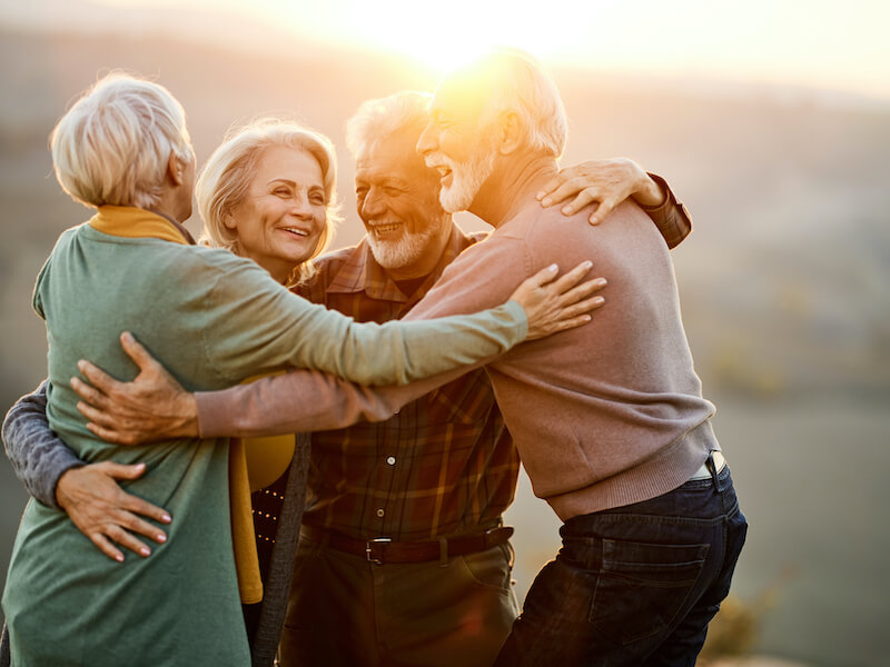 Group of happy seniors enjoying in embrace during sunset. 