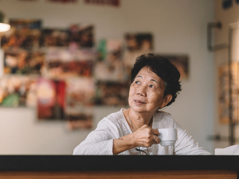 Asian woman drinking coffee and straining to hear the birds outside.